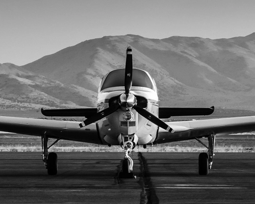 black and white photo of an airplane in front of mountains prior to take-off.